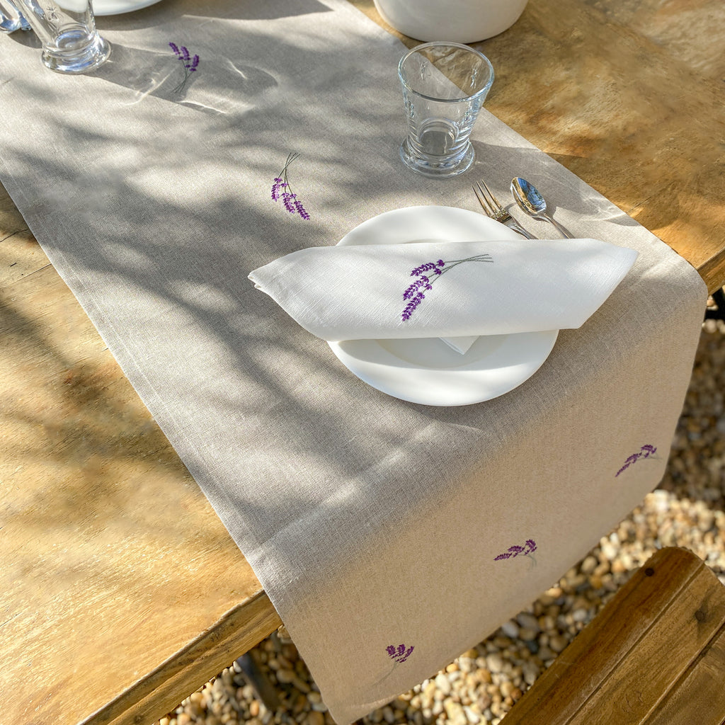 Beigefarbener Tischläufer aus Leinen mit fein gestickten Lavendelmustern.