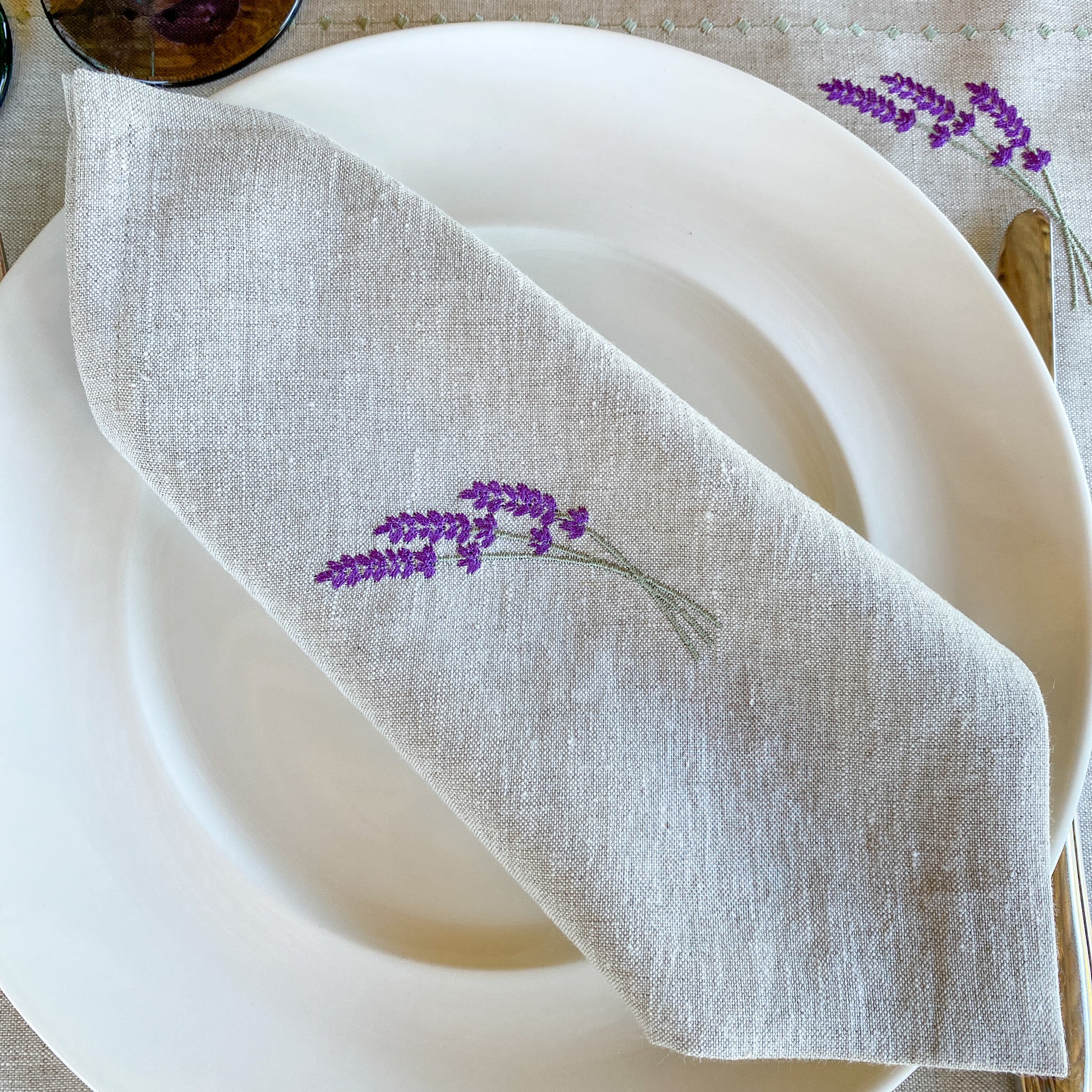 Leinenserviette mit zarter Lavendelstickerei, handgefertigt in unseren Werkstätten in Südfrankreich. Präsentiert auf einem stilvoll gedeckten Tisch – ideal für eine natürliche, elegante Tischdekoration.