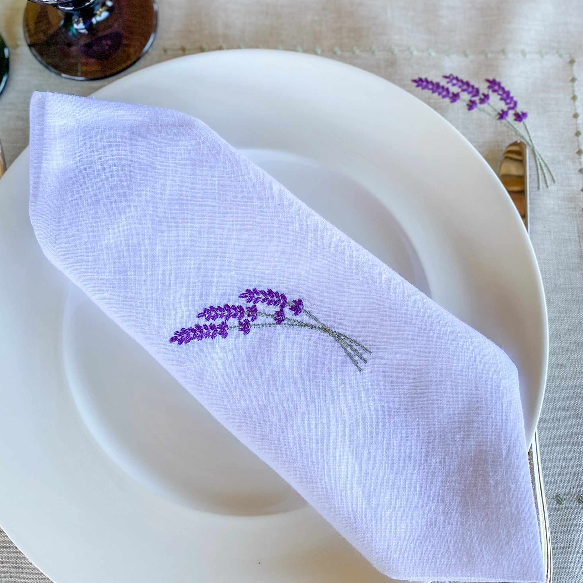 Leinenserviette mit zarter Lavendelstickerei, handgefertigt in unseren Werkstätten in Südfrankreich. Präsentiert auf einem stilvoll gedeckten Tisch – ideal für eine natürliche, elegante Tischdekoration.